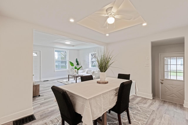 dining area featuring light wood finished floors, baseboards, a tray ceiling, and visible vents
