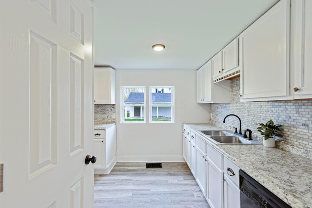 kitchen featuring light wood finished floors, dishwasher, a sink, tasteful backsplash, and white cabinetry