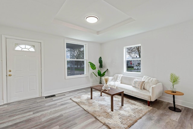 living area featuring a tray ceiling, light wood-style floors, visible vents, and baseboards