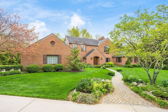view of front of house featuring a chimney, a front lawn, and brick siding
