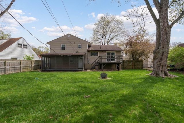 rear view of property featuring a wooden deck, a fenced backyard, a fire pit, and a sunroom