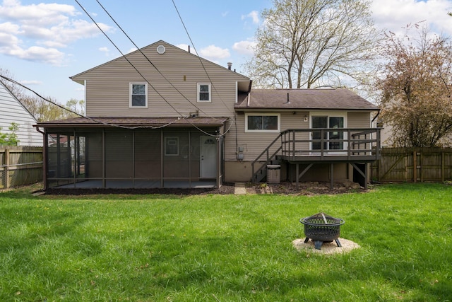 rear view of house with a fenced backyard, a fire pit, a deck, a yard, and a sunroom