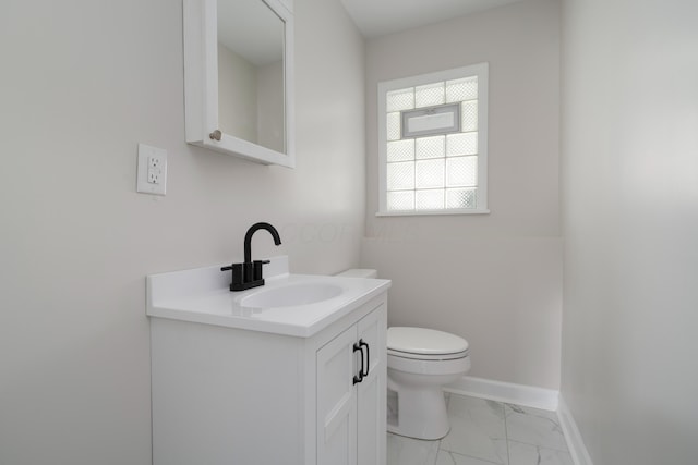 half bathroom with baseboards, marble finish floor, vanity, and toilet