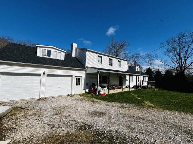 view of front of home with gravel driveway, a chimney, an attached garage, covered porch, and a front yard
