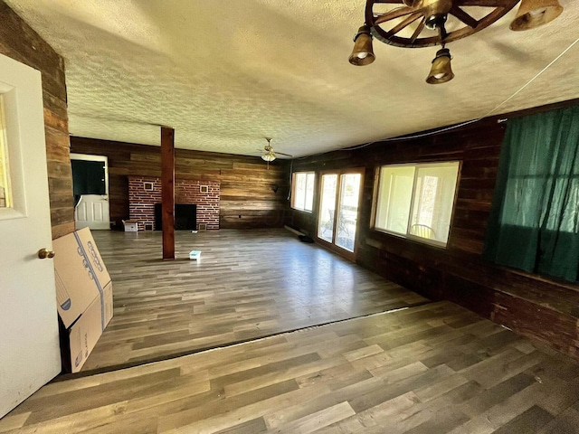 unfurnished living room with wooden walls, wood finished floors, a brick fireplace, a textured ceiling, and ceiling fan