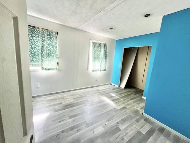 unfurnished bedroom featuring baseboards, wood finished floors, a textured ceiling, and a closet