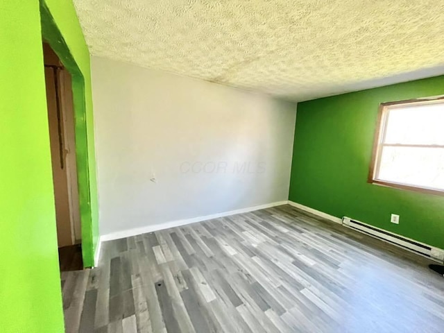unfurnished room featuring a baseboard heating unit, baseboards, wood finished floors, and a textured ceiling