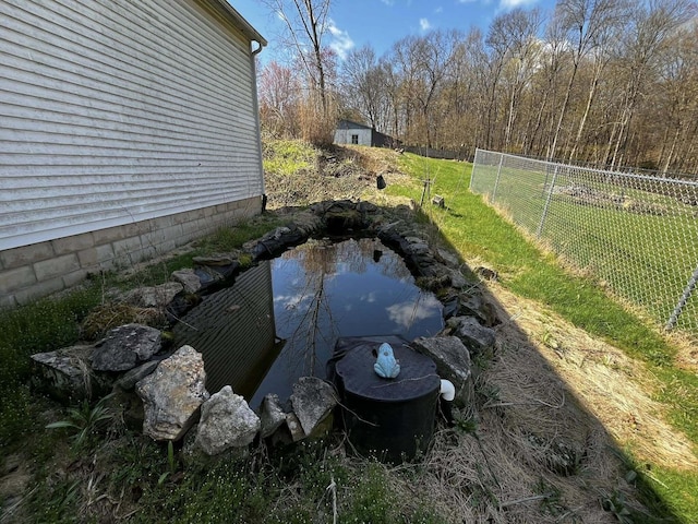 view of yard featuring an outbuilding, fence, and a garden pond