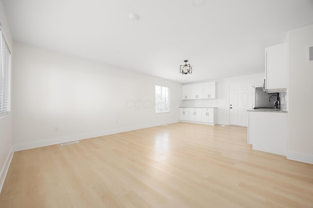 unfurnished living room with light wood finished floors, baseboards, and a sink