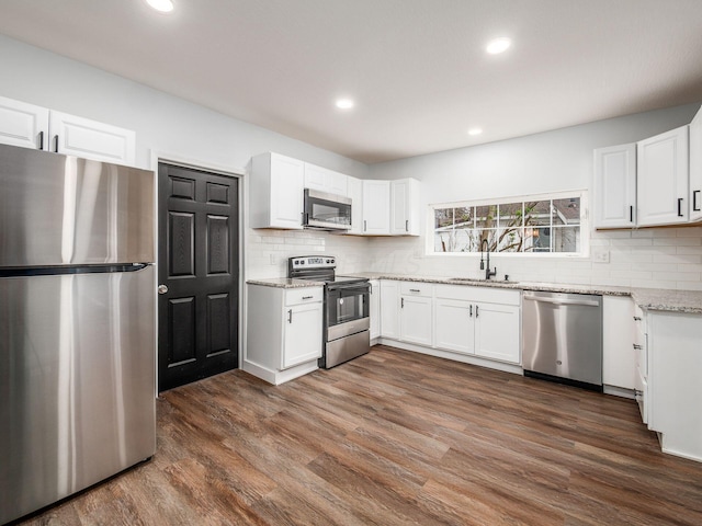 kitchen featuring dark wood-style floors, a sink, decorative backsplash, light stone counters, and appliances with stainless steel finishes