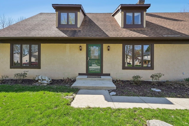 view of front of home with stucco siding, a shingled roof, and a front yard