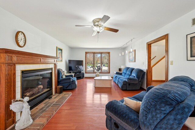 living area featuring a tile fireplace, ceiling fan, rail lighting, and wood finished floors