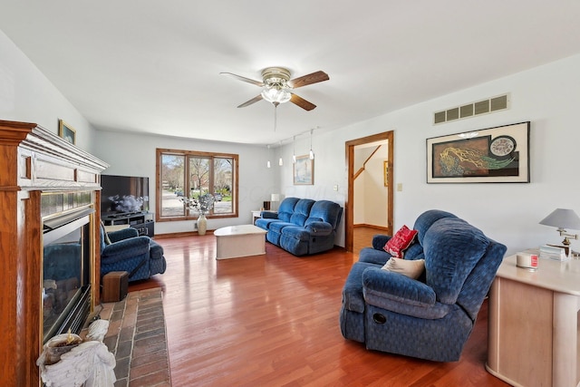 living room featuring a ceiling fan, a glass covered fireplace, wood finished floors, and visible vents