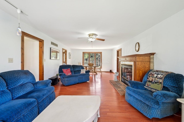 living room with a glass covered fireplace, wood finished floors, visible vents, and a ceiling fan