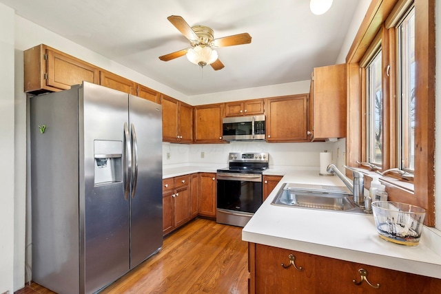 kitchen featuring brown cabinets, stainless steel appliances, light countertops, a ceiling fan, and a sink