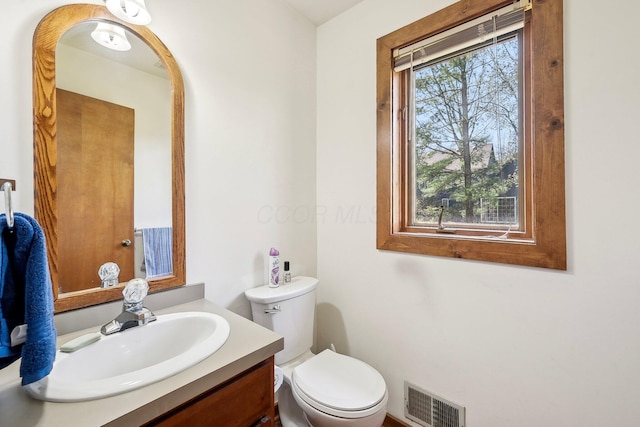 half bathroom with toilet, vanity, and visible vents