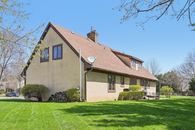 rear view of house featuring a lawn, a chimney, roof with shingles, and stucco siding