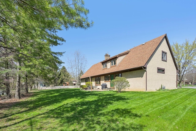 rear view of house with fence, a lawn, a chimney, and stucco siding