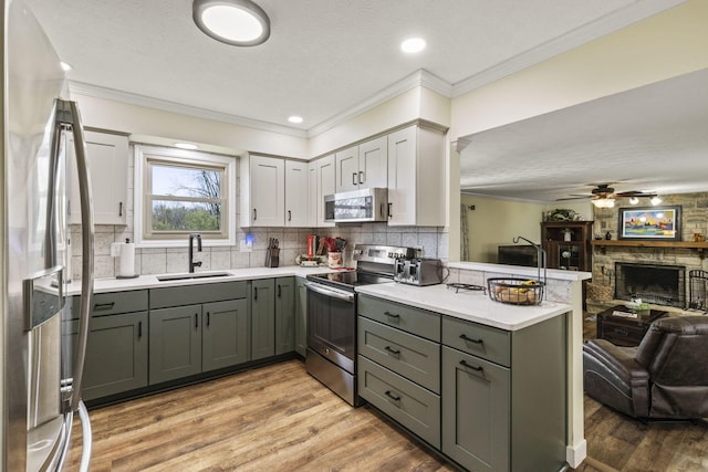 kitchen featuring a peninsula, a sink, open floor plan, gray cabinets, and appliances with stainless steel finishes