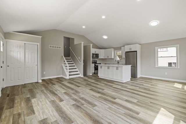 unfurnished living room featuring a sink, light wood-type flooring, baseboards, visible vents, and lofted ceiling