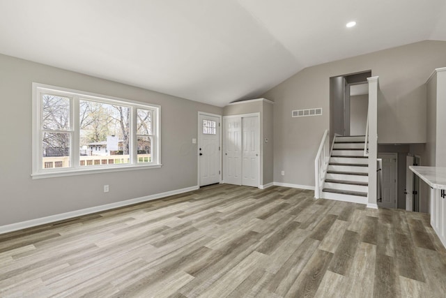 unfurnished living room featuring vaulted ceiling, visible vents, light wood-type flooring, baseboards, and stairs