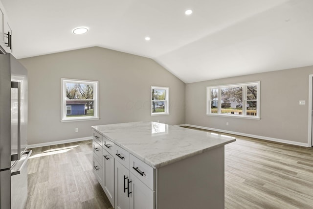 kitchen featuring recessed lighting, light stone counters, light wood-type flooring, a center island, and baseboards