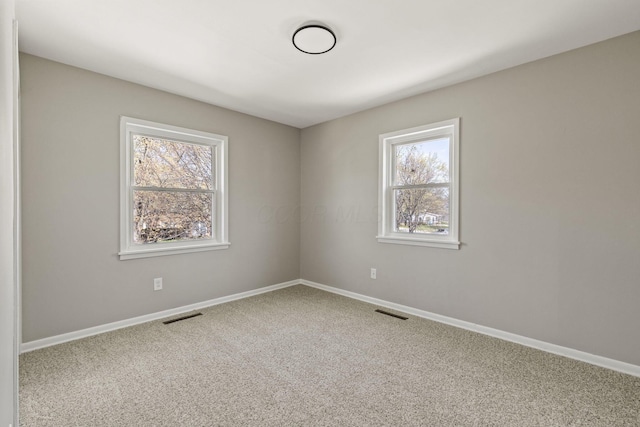 carpeted spare room featuring baseboards, visible vents, and a wealth of natural light
