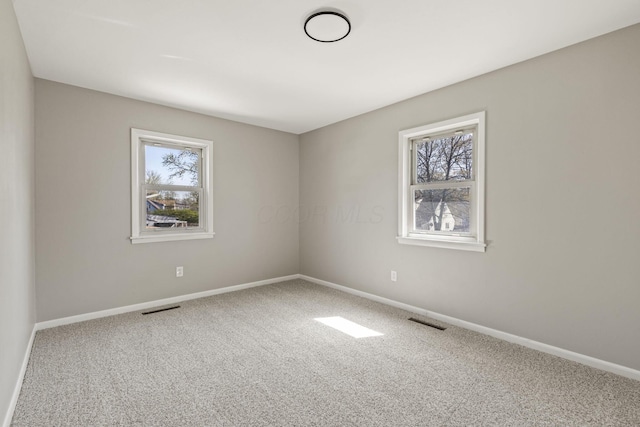 empty room with carpet, visible vents, and baseboards