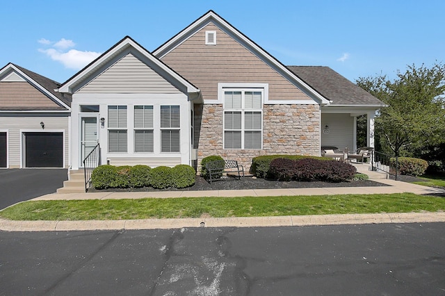 craftsman house with a porch, driveway, stone siding, and a garage