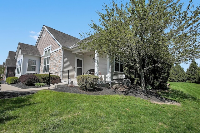 view of side of property with a yard, roof with shingles, stone siding, and covered porch
