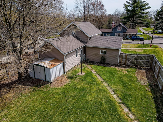 exterior space with a storage shed, a lawn, a fenced backyard, an outdoor structure, and roof with shingles