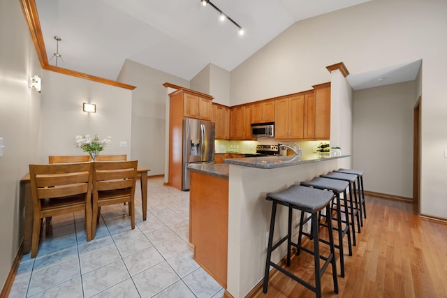 2882 Kool Air Way, Columbus, OH 43231 - kitchen with stainless steel appliances, a peninsula, brown cabinetry, a breakfast bar, and high vaulted ceiling