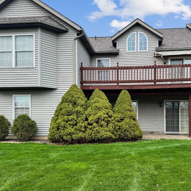 back of property with a wooden deck, roof with shingles, and a yard