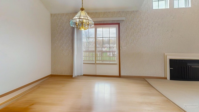 unfurnished dining area featuring baseboards, a notable chandelier, wood finished floors, and a healthy amount of sunlight