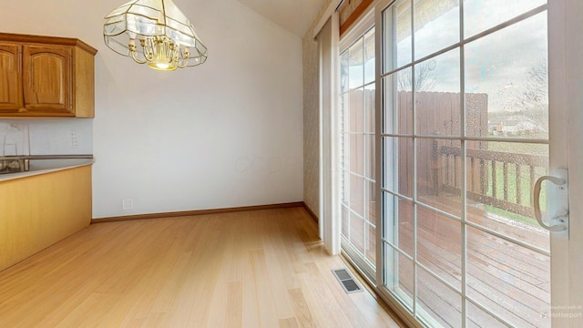 unfurnished dining area featuring a notable chandelier, light wood-type flooring, baseboards, lofted ceiling, and visible vents