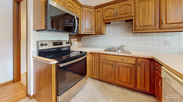 kitchen featuring light countertops, brown cabinetry, appliances with stainless steel finishes, and a sink