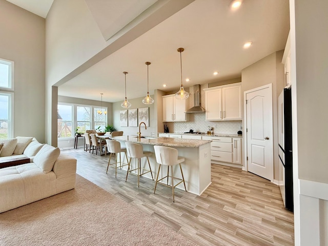 kitchen with wall chimney range hood, stainless steel gas cooktop, open floor plan, a breakfast bar area, and light wood-style flooring