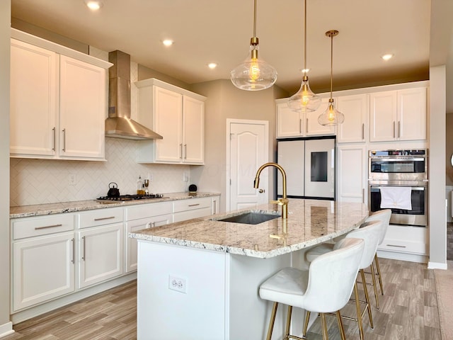 kitchen featuring wall chimney exhaust hood, a sink, light wood-style floors, and appliances with stainless steel finishes
