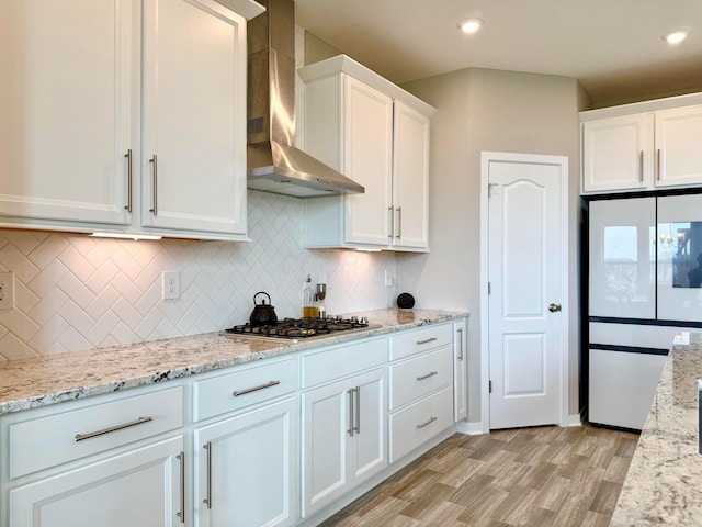 kitchen with wall chimney exhaust hood, white cabinets, stainless steel gas cooktop, freestanding refrigerator, and light wood-style floors