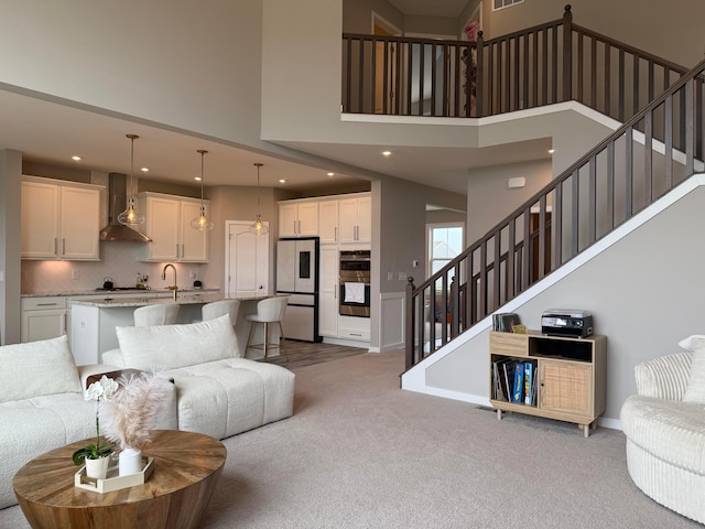 carpeted living area featuring recessed lighting, a towering ceiling, visible vents, baseboards, and stairs