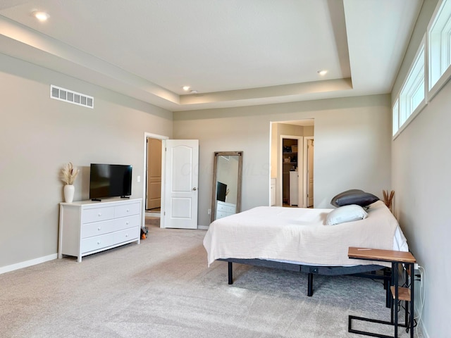 bedroom with baseboards, visible vents, light colored carpet, and a tray ceiling
