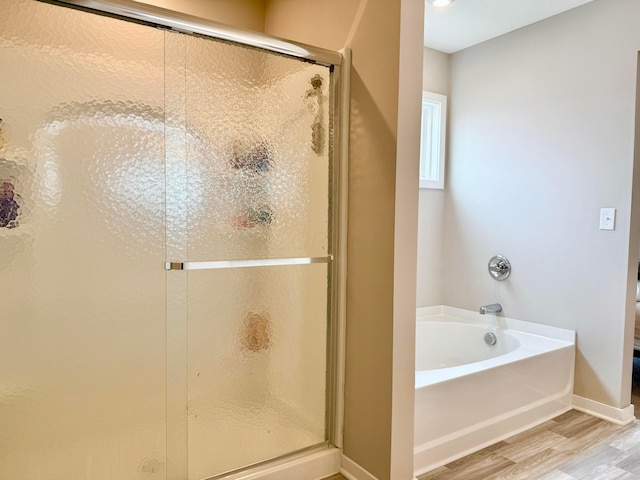 bathroom with a shower stall, a garden tub, wood finished floors, and baseboards