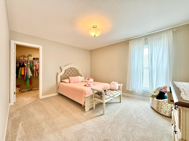 bedroom with light colored carpet, baseboards, and a spacious closet