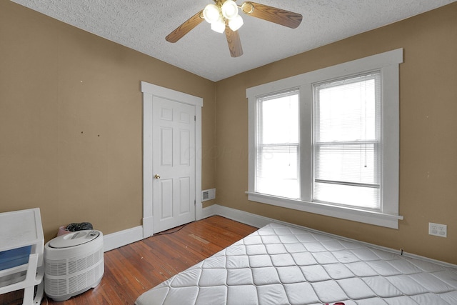 bedroom with baseboards, wood finished floors, a textured ceiling, and visible vents