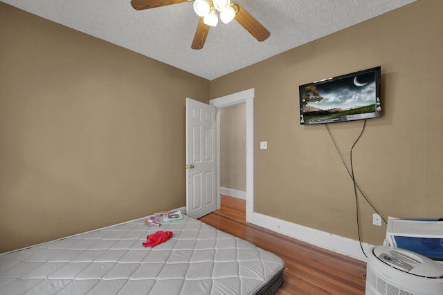bedroom featuring wood finished floors, a textured ceiling, a ceiling fan, and baseboards