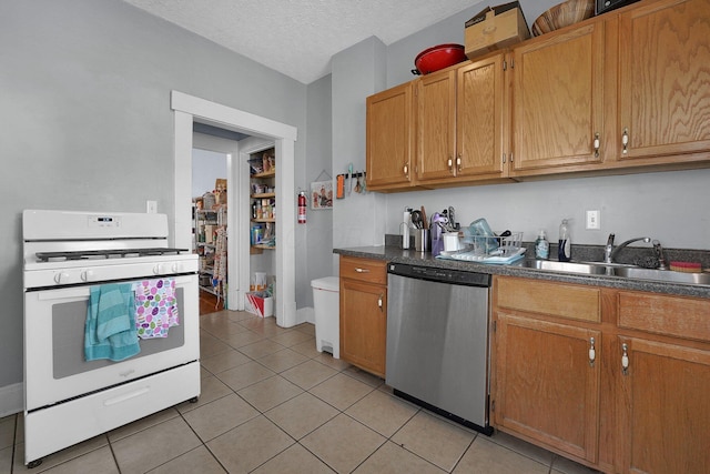kitchen featuring white range with gas cooktop, dark countertops, stainless steel dishwasher, and a sink