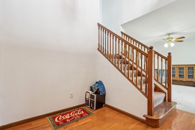 stairs with wood finished floors, a ceiling fan, and baseboards