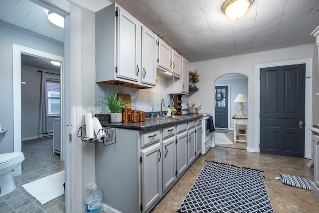kitchen featuring dark countertops, a sink, arched walkways, tasteful backsplash, and white cabinetry