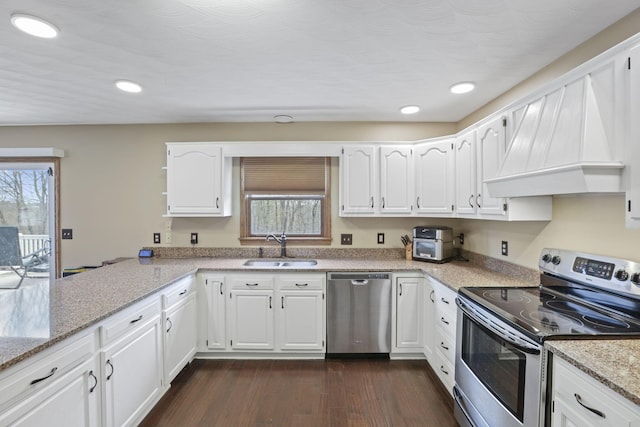 kitchen featuring stainless steel appliances, a sink, white cabinetry, custom range hood, and light stone countertops