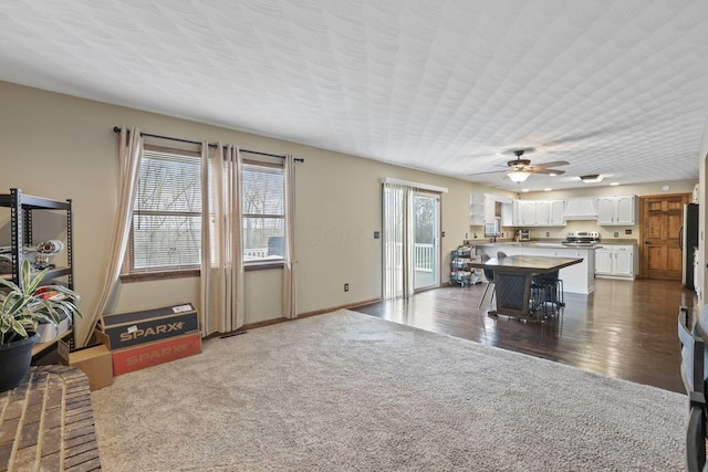 living room featuring a ceiling fan, baseboards, and dark carpet